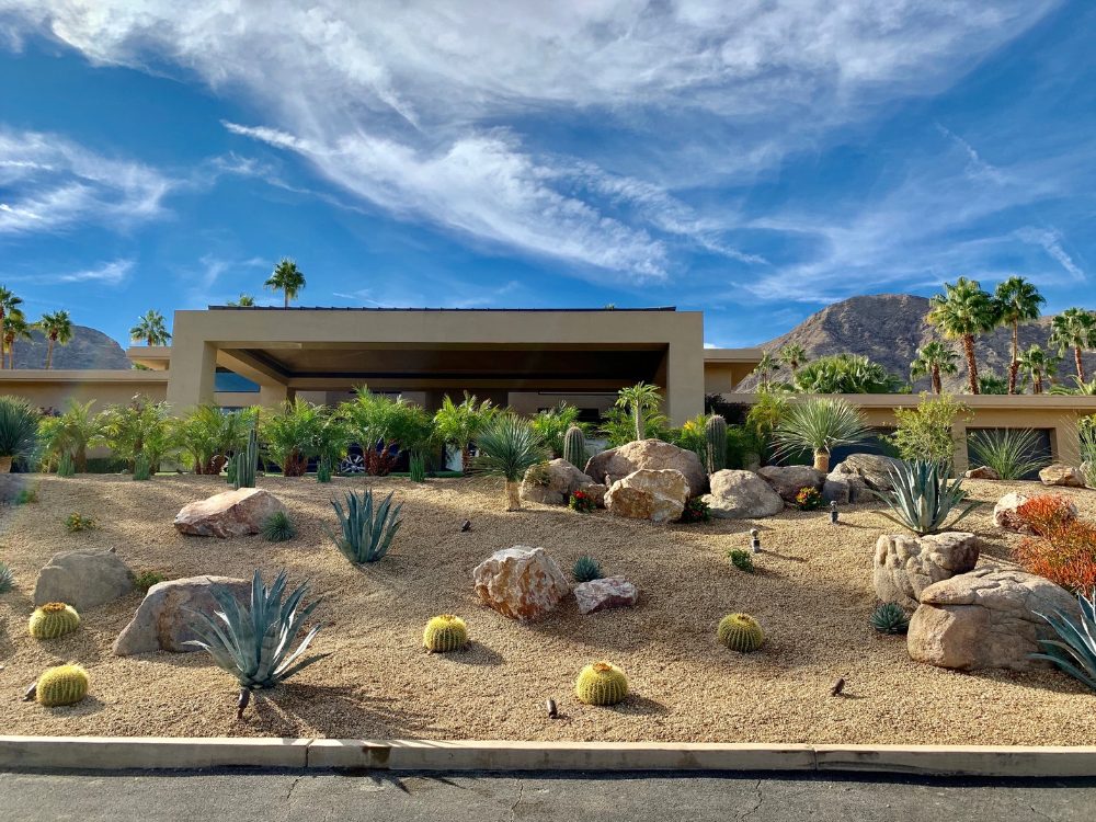 Desert landscape with gravel, boulders and barrel cactus in front of a modern home